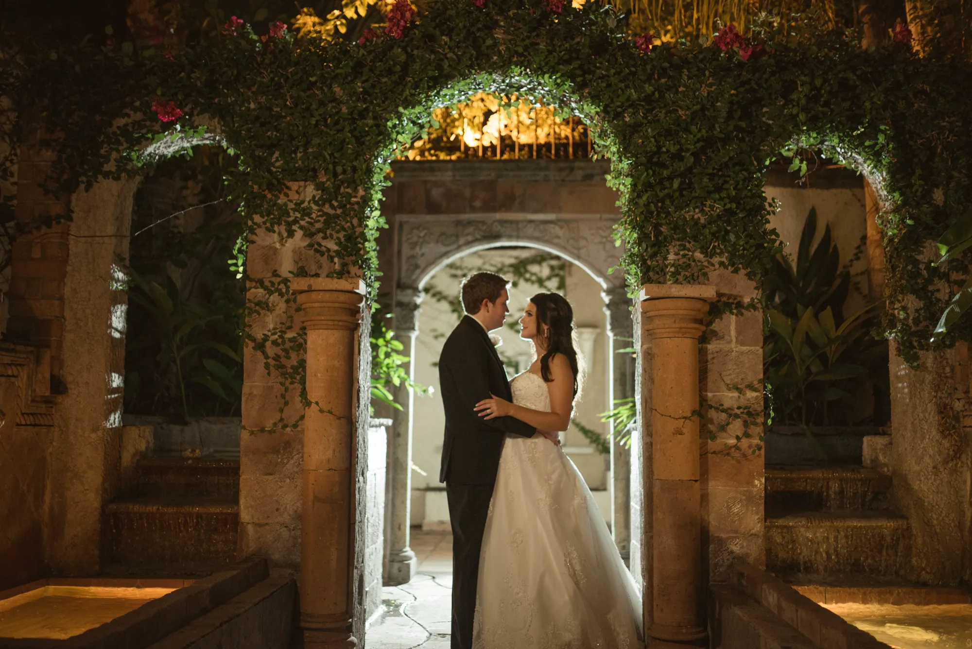 Couple embracing beneath an ivy-covered stone arch at night