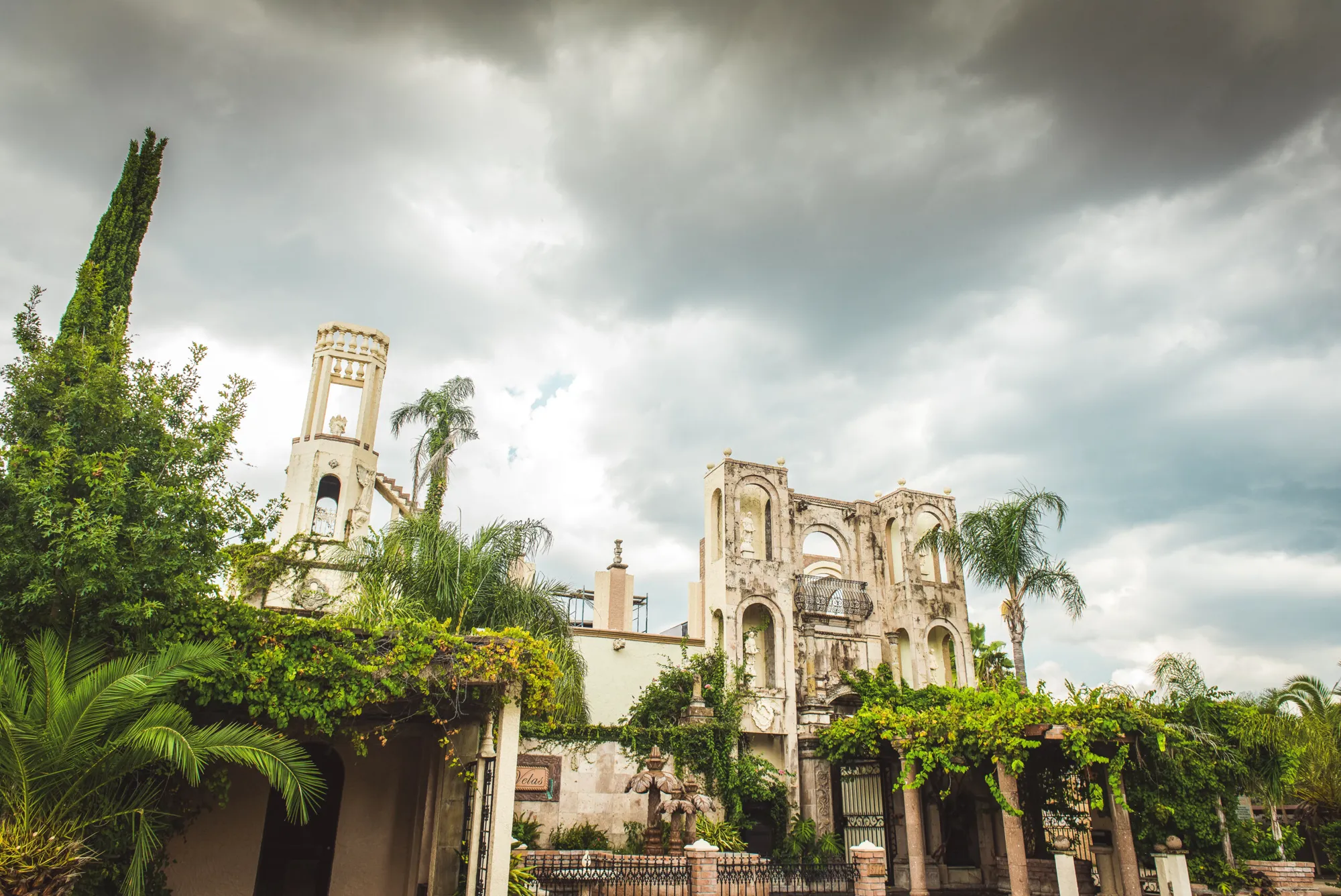 Courtyard greenery and bell tower under a cloudy sky